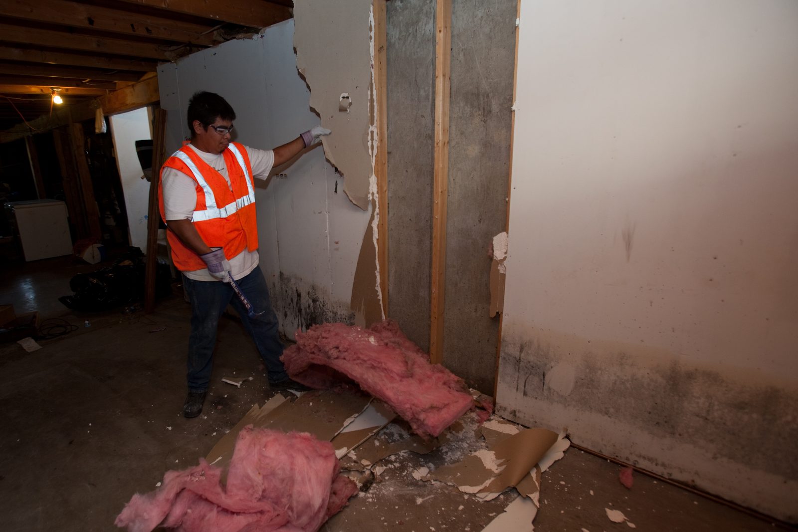 Calumet Restoration Co technician in a high-visibility vest pulling wet drywall and insulation from a basement wall in Flossmoor