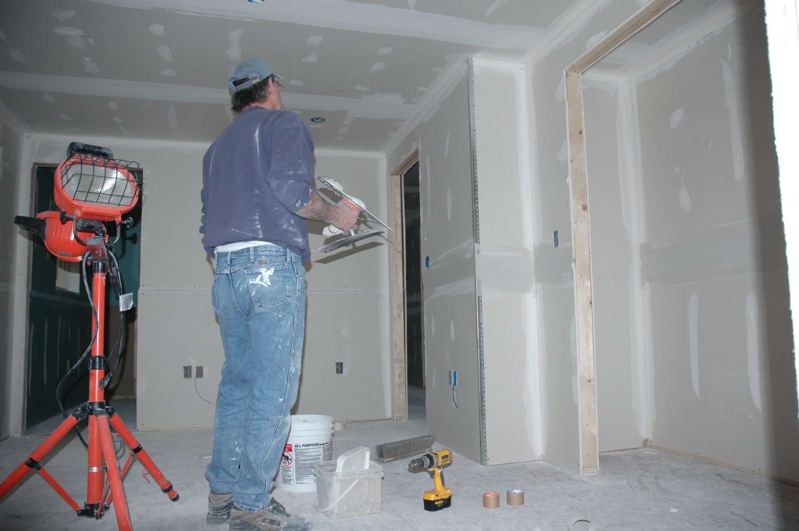 Technician finishing new drywall in a Flossmoor basement under a work light